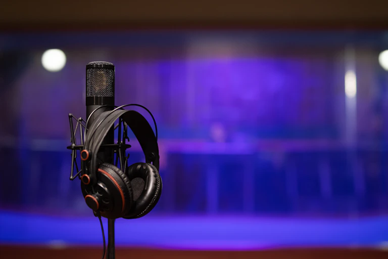 A pair of black headphones hang on a microphone stand.