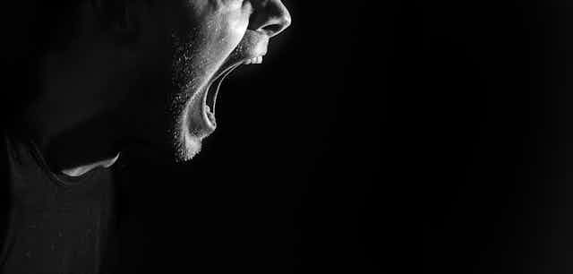 Close up of a man shouting with his mouth wide open, against a black background
