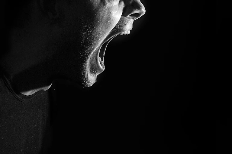 Close up of a man shouting with his mouth wide open, against a black background