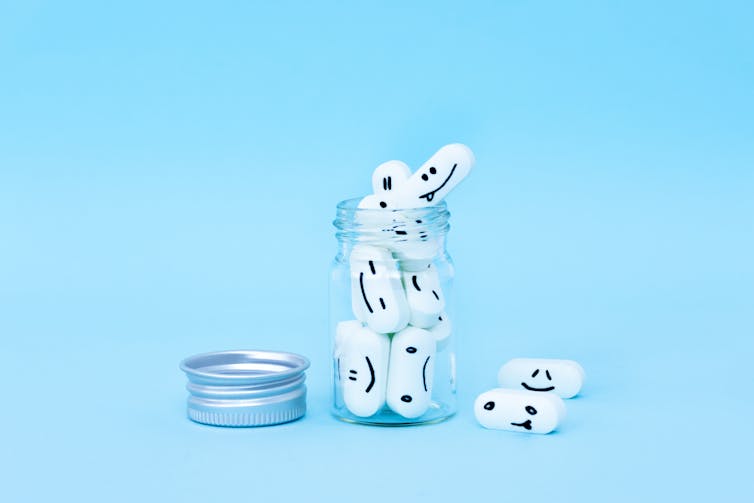 A jar of 'happy pills' sits against a light blue background, with a silver cap unscrewed