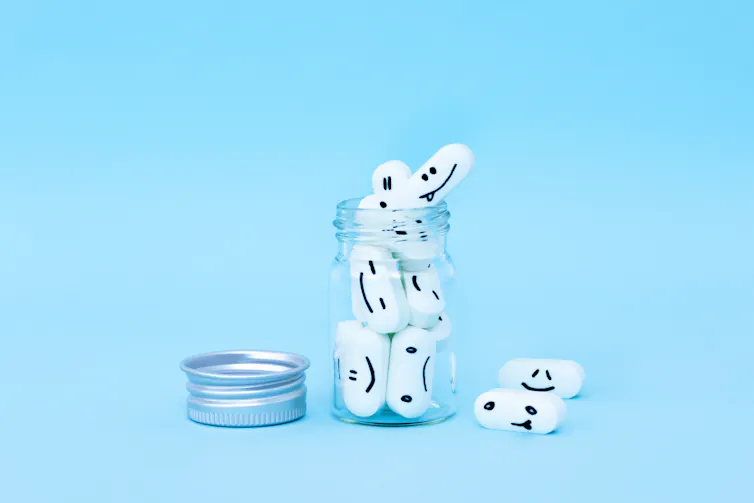 A jar of 'happy pills' sits against a light blue background, with a silver cap unscrewed