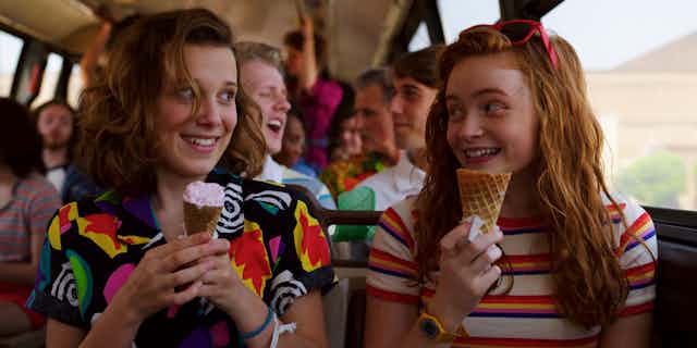 Two teenaged girls eating ice cream on a bus