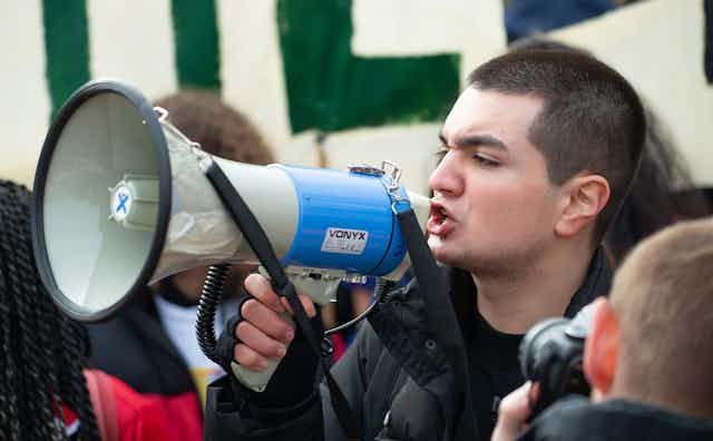 A person facing to the left of the image shouts into a megaphone they are holding