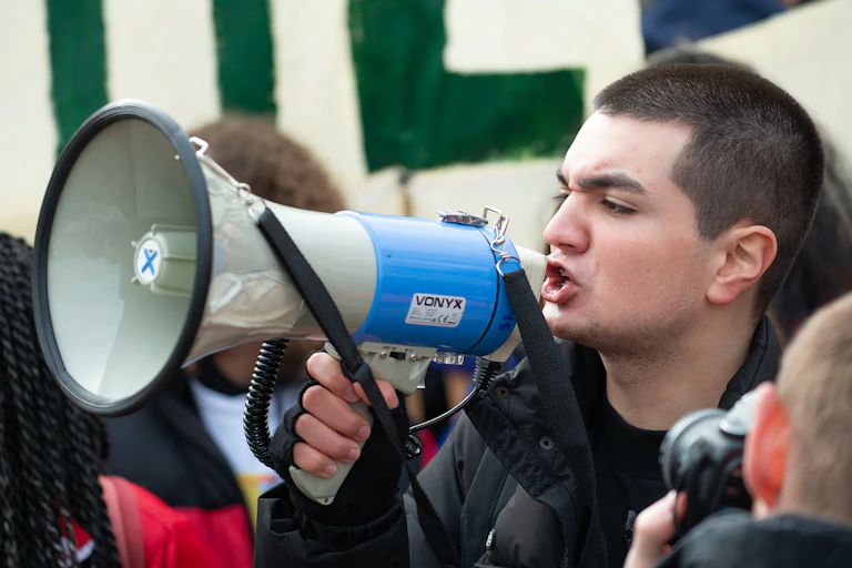 A person facing to the left of the image shouts into a megaphone they are holding