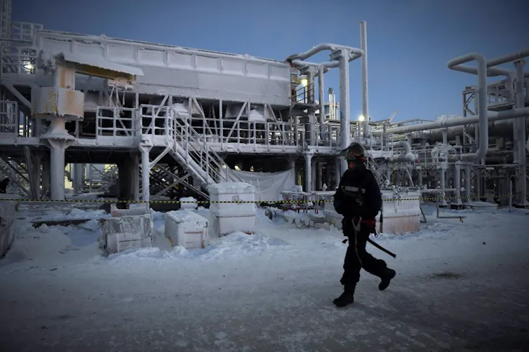 Une usine enneigée en fin de journée, un homme armé marche devant l’usine
