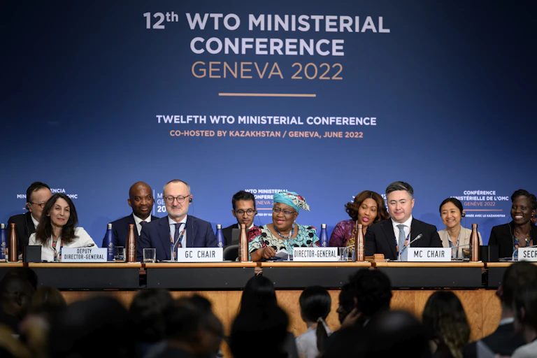 A panel of ministers are seated a table with a backdrop that reads 12th WTO Ministerial Conference Geneva 2022.