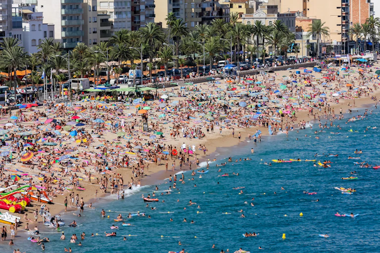 Crowds on a sandy beach at the height of summer, seen from above.