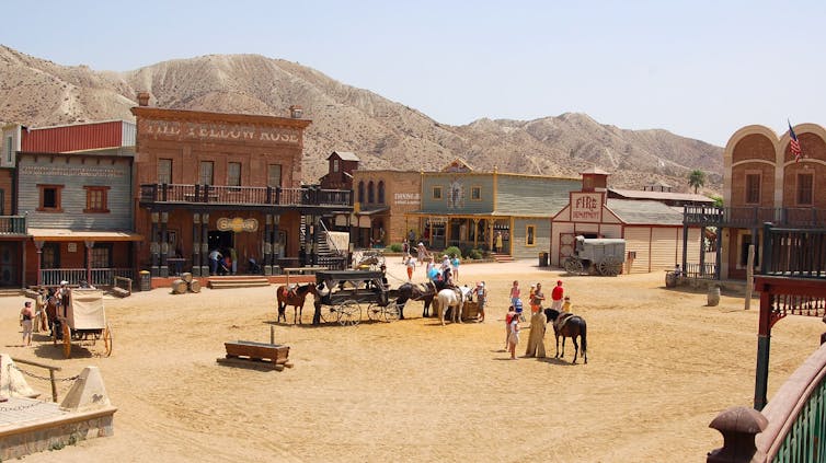 A dusty western scene of a town square with mountains in the background.