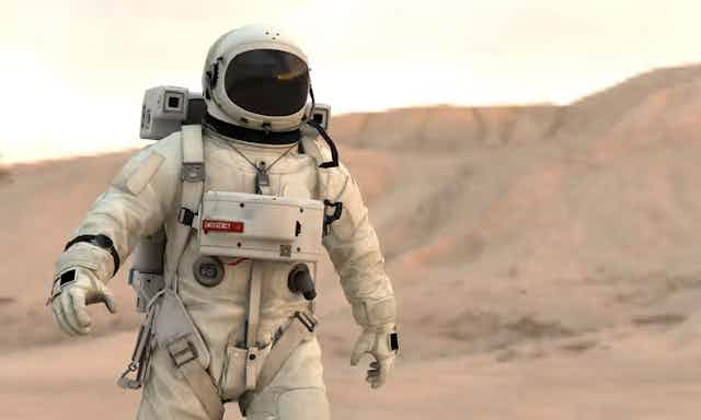 Dengan latar belakang bukit berwarna merah muda, seorang astronot berjalan di tanah Mars.