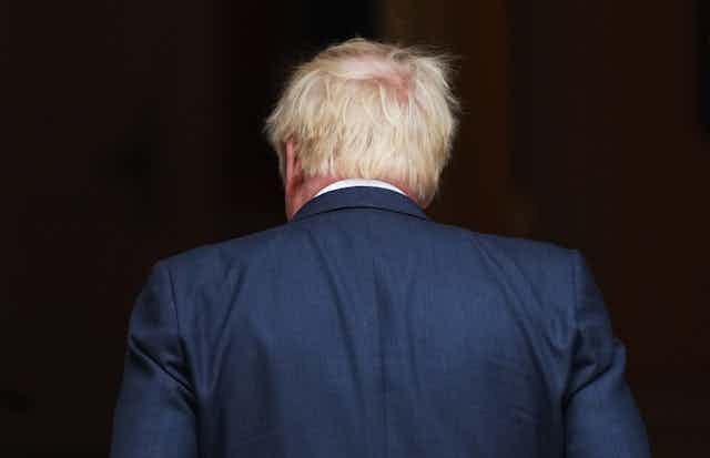 Boris Johnson with is seen with his back to the camera wearing a blue suit with trademark messy blond hair