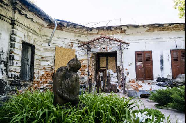 a damaged courtyard with boarded up windows and a statue int he foreground