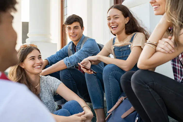 Groupe de jeunes amis heureux assis dans la cour du lycée et parlant