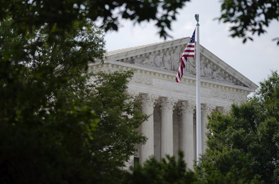 An American flag flutters outside the Supreme Court, frammed by green leafs of nearby trees.