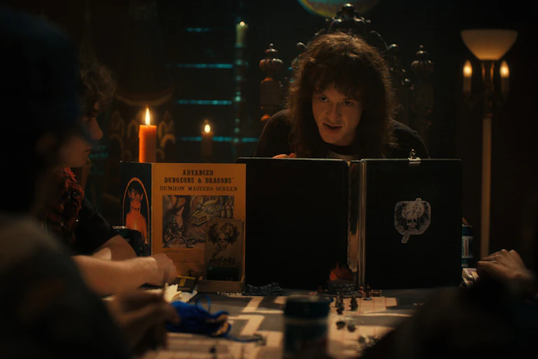 A man with long hair sits behind a book with a candle in the corner
