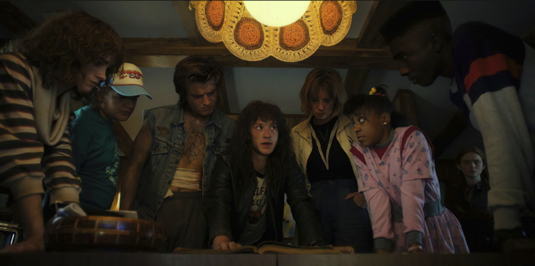 A group of people crowd a table as one person reads.