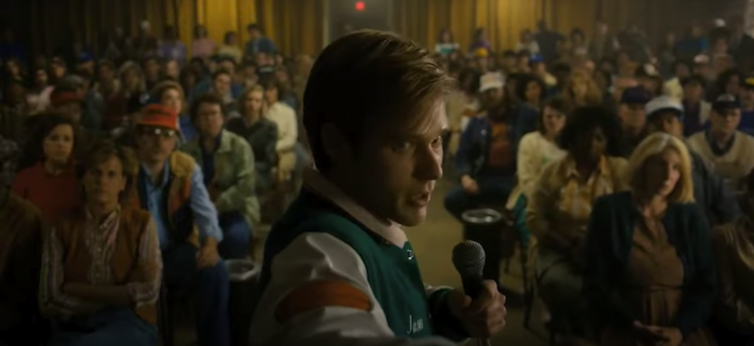 A man in a high school jacket stands in front of a crowd