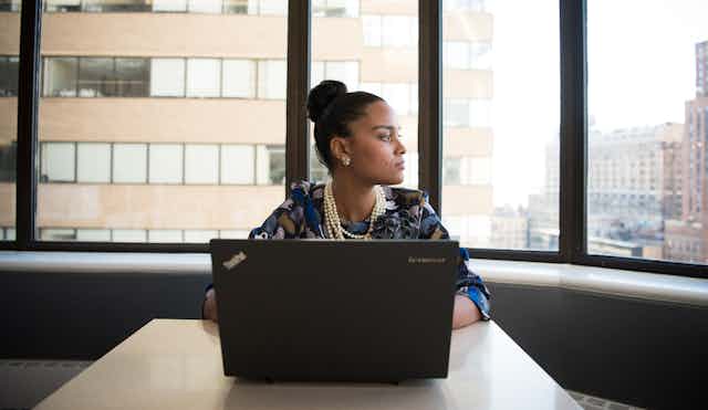 Woman at laptop with tall buildings behind her