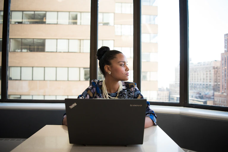 Woman at laptop with tall buildings behind her