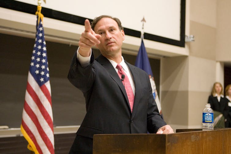 A man standing next to the US flag pointing his finger.