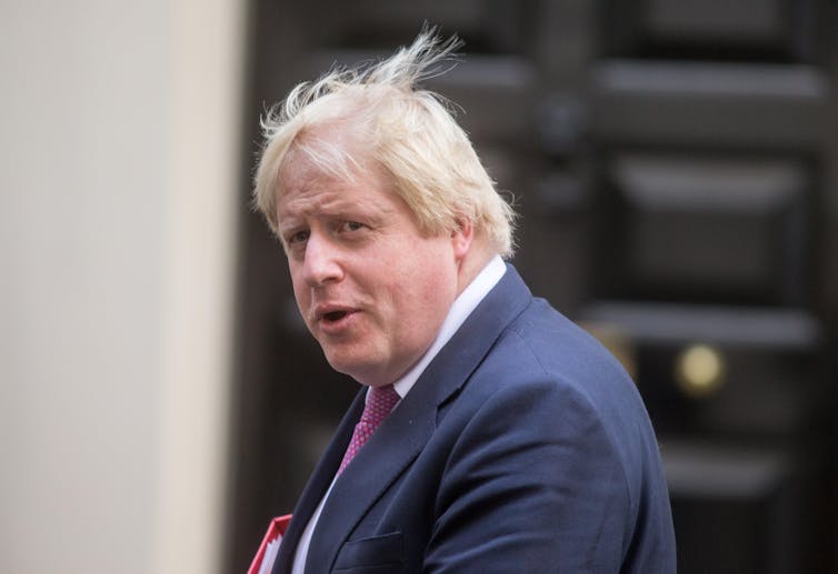 A close up shot of Boris Johnson outside, in a blue suit and magenta tie.