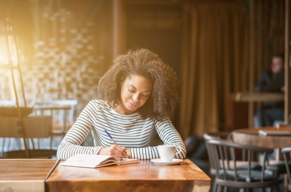 Young woman sitting in a cafe writes in a notebook.