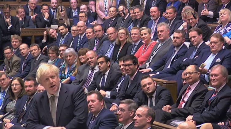 A crowd of people in suits, seated, with Boris Johnson standing in the foreground.