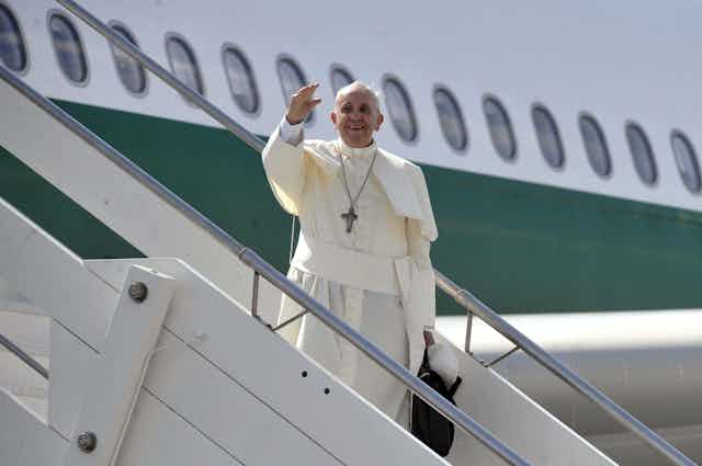 Pope Francis standing and waving from the steps of an aeroplane.