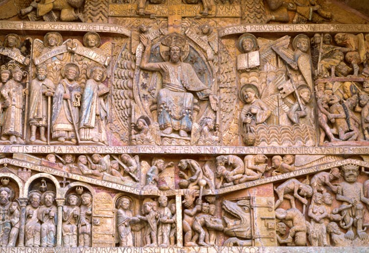 A carving on the side of a church shows many small human figures with Jesus sitting in the middle.