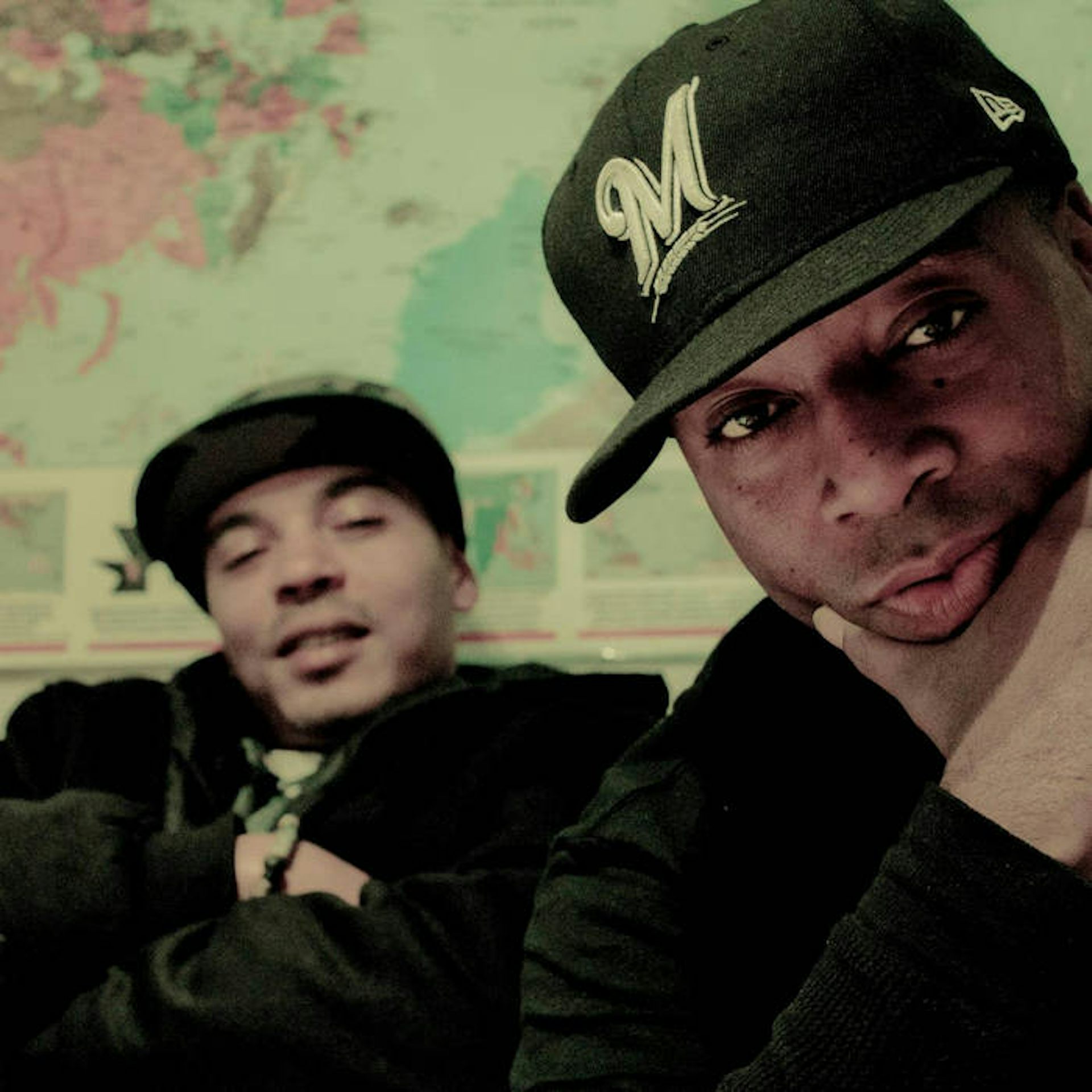Two Black men look directly at the camera against the backdrop of a world map.