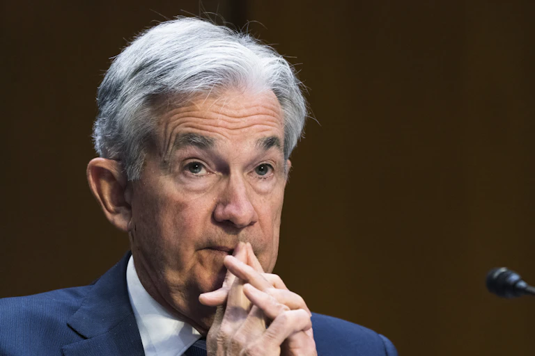 A white man with gray hair holds his hands clasped at his lips