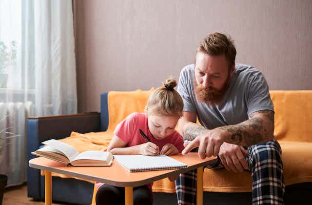 A father works with his daughter on a writing task.