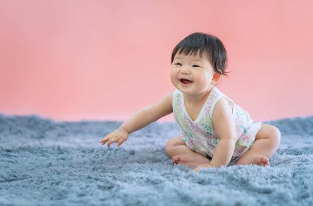 Baby girl in a floral dress smiled widely, sitting on a shaggy grey rug