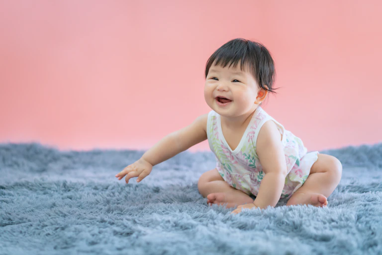 Baby girl in a floral dress smiled widely, sitting on a shaggy grey rug