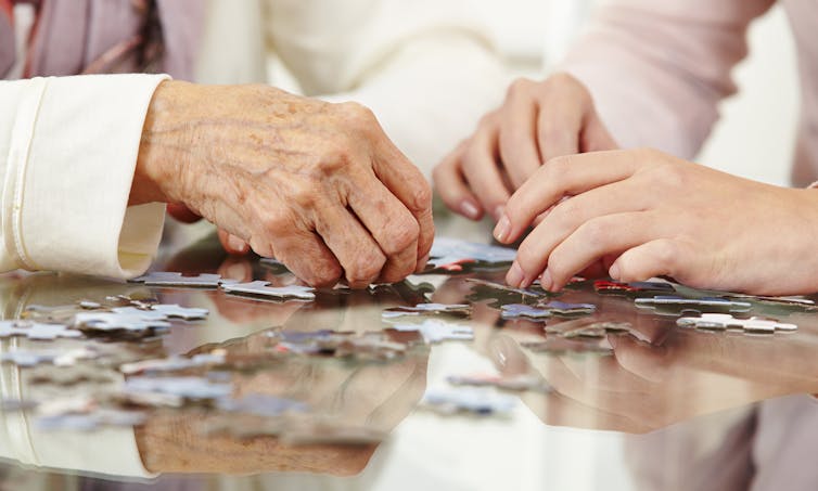 pair of old hands and pair of younger hands doing puzzle
