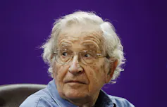 An elderly man with grey hair and glasses looks to the right.