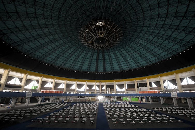 Rows of beds are seen under the domed ceiling of a convention centre.