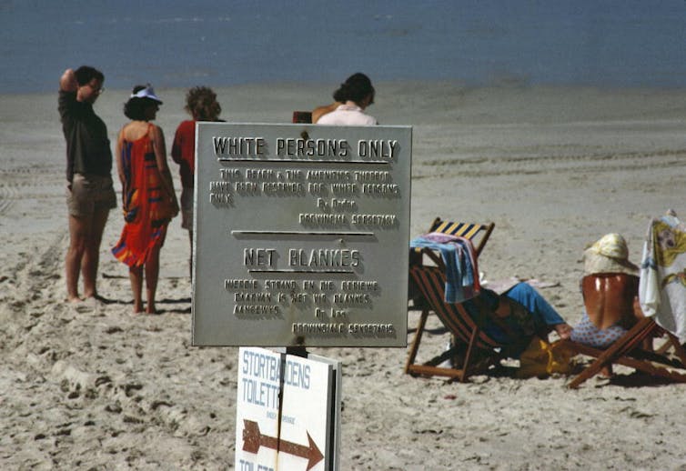 A sign on a beach with people in the background.