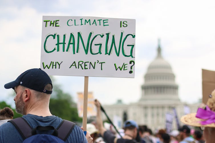 a man holding a sign reading THE CLIMATE IS CHANGING WHY AREN'T WE
