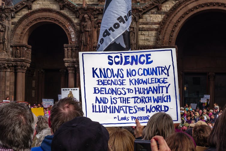 protesters holding a sign with a Louis Pasteur quote that begins SCIENCE KNOW NO COUNTRY