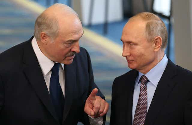 Two men in dark suits and ties, with one talking to the other.