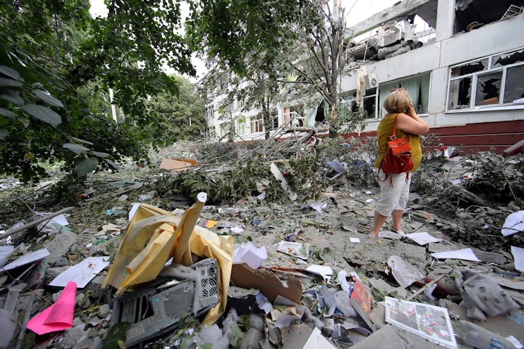 A woman stands, hand to face in the rubble of a building destroyed in Ukraine by Russian forces.