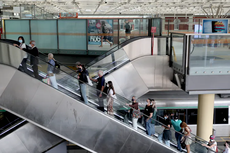 people in masks go up escalator