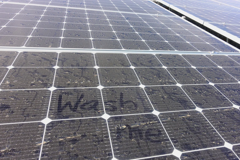 A dusty solar panel with 'wash me' written into it
