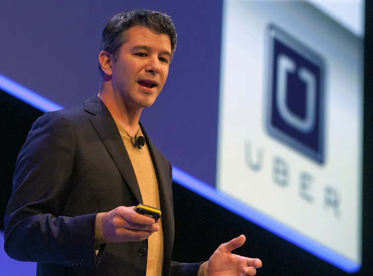 Travis Kalanick speaking on stage with the Uber logo on a screen behind him.