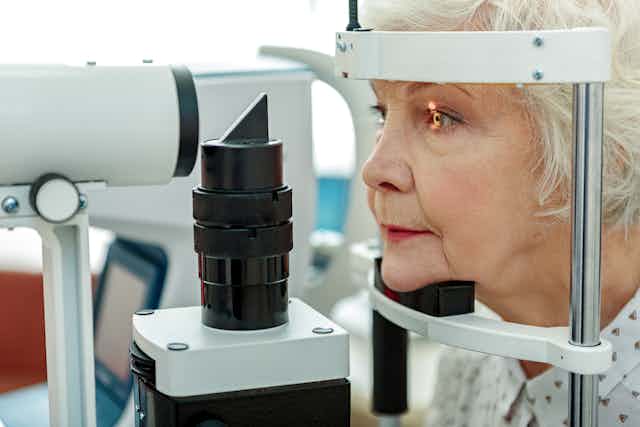 An elderly woman looks into a bright light during an eye exam at an optometrist's.