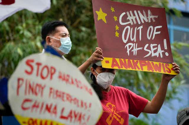 Two men wearing masks hold protest signs. One reads China Out of Ph Sea.