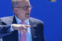A grey-haired man in glasses points as he walks into a summit.