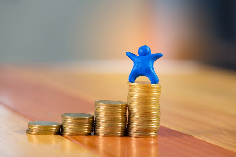 Blue plasticine 'human' figure on pile of coins.