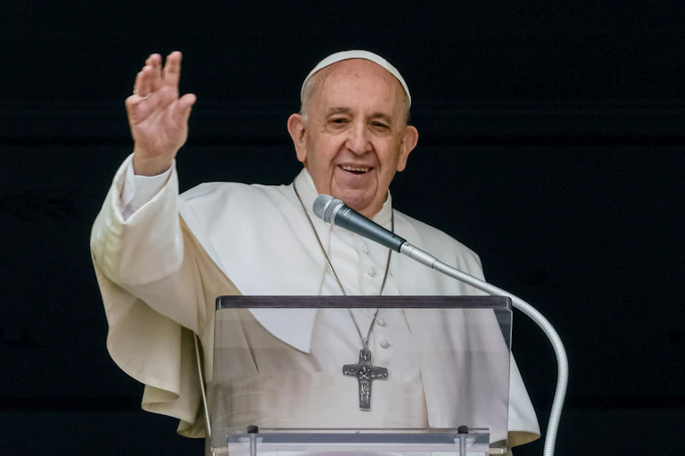 Le pape François, souriant, tend le bras