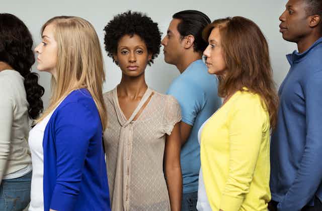A Black woman looks straight at the camera while people of various ethnicities look to the left.